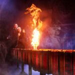 Albus and Scorpius cower in the right side of the photo, looking at a fire in the centre stage. The fire and the boys stand on top of a long row of suitcases.