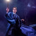 Harry Potter in the Forbidden Forest. His robes are billowing and he holds his wand out that is lit up